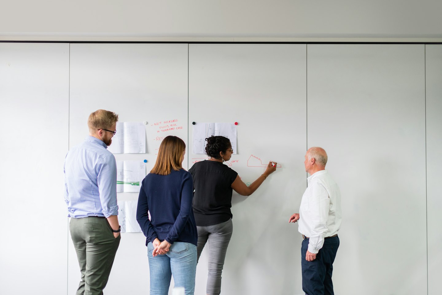 Business team collaborates on a red diagram on a whiteboard.